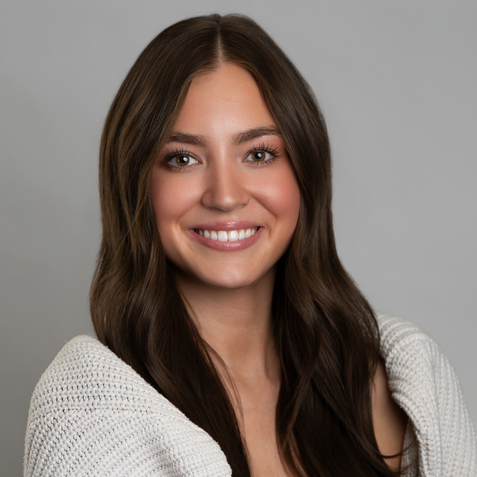 A portrait of a smiling woman with long brown hair wearing a white knit sweater. -JRPMTS LLC