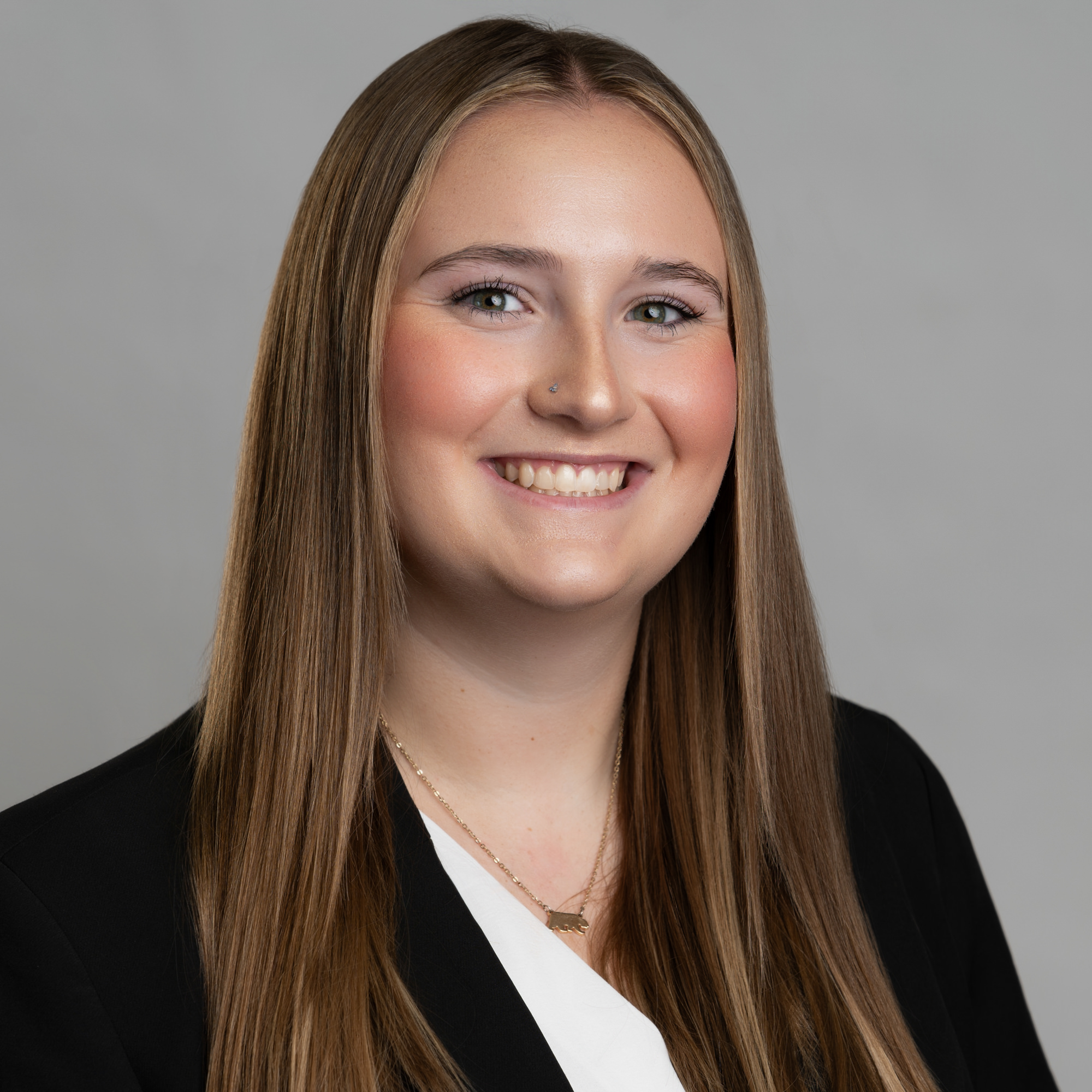 Headshot of a smiling young woman with long hair wearing a black blazer and a necklace. -JRPMTS LLC