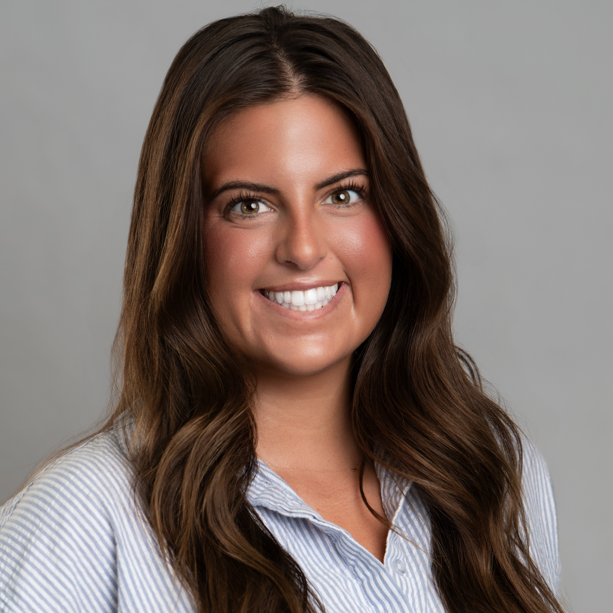 Headshot of a smiling woman with long brown hair wearing a light blue and white striped button-down shirt. -JRPMTS LLC